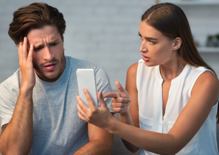 Párkapcsolati konfliktus: nő telefonon mutat valamit a férfinak, aki aggódva reagál